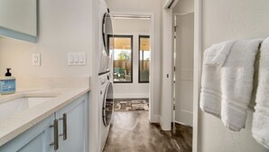 A narrow hallway with a washing machine, a sink with a soap dispenser, and a door leading to a room with a view.