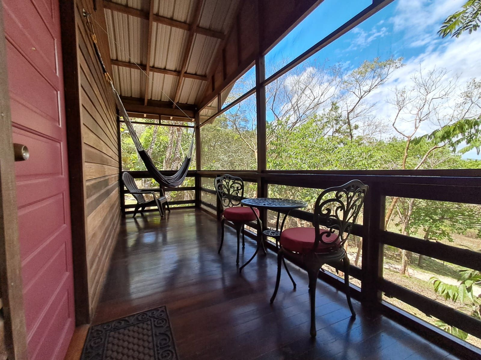 A covered outdoor seating area with a hammock, two chairs, and a table.