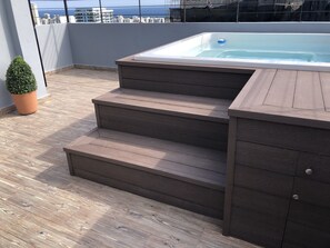 Terraza en la azotea con jacuzzi, escalones de madera y una planta en maceta.
