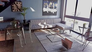 Ett modernt vardagsrum med en grå soffa, ett soffbord i genomskinligt glas och ett stort fönster.