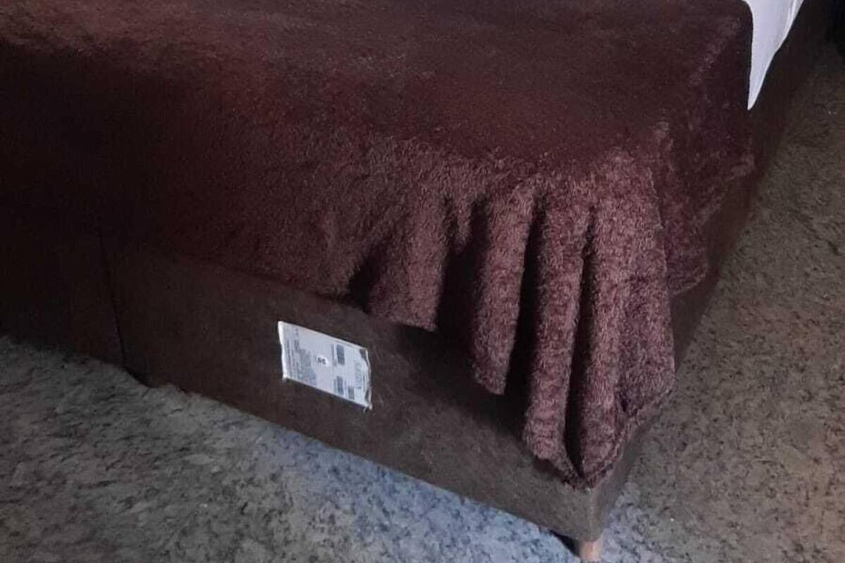 A bed with white bedding and a brown throw blanket, a nightstand, and a wall-mounted light switch.