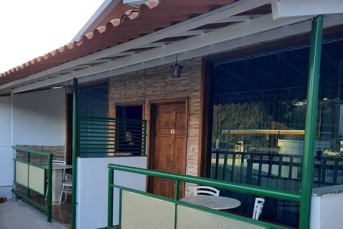 A building with a covered outdoor area featuring a table and chairs, a wooden door, and a green metal railing.