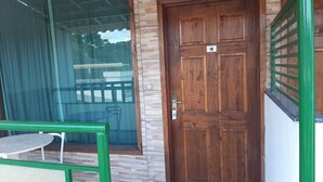 Una puerta de madera con una placa de número, una puerta de cristal con marco metálico y una barandilla verde.