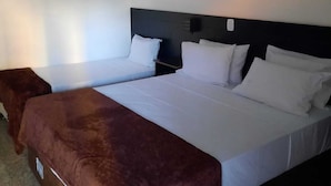 Habitación de hotel con dos camas, una manta marrón, cabecero, unidad de aire acondicionado y cortina.