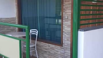 Um quarto com piso de madeira, geladeira branca, portão de metal verde e janela com cortina.