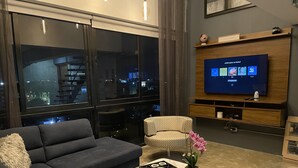 A modern living room with a large TV, a sofa, a chair, and a coffee table with a board game.