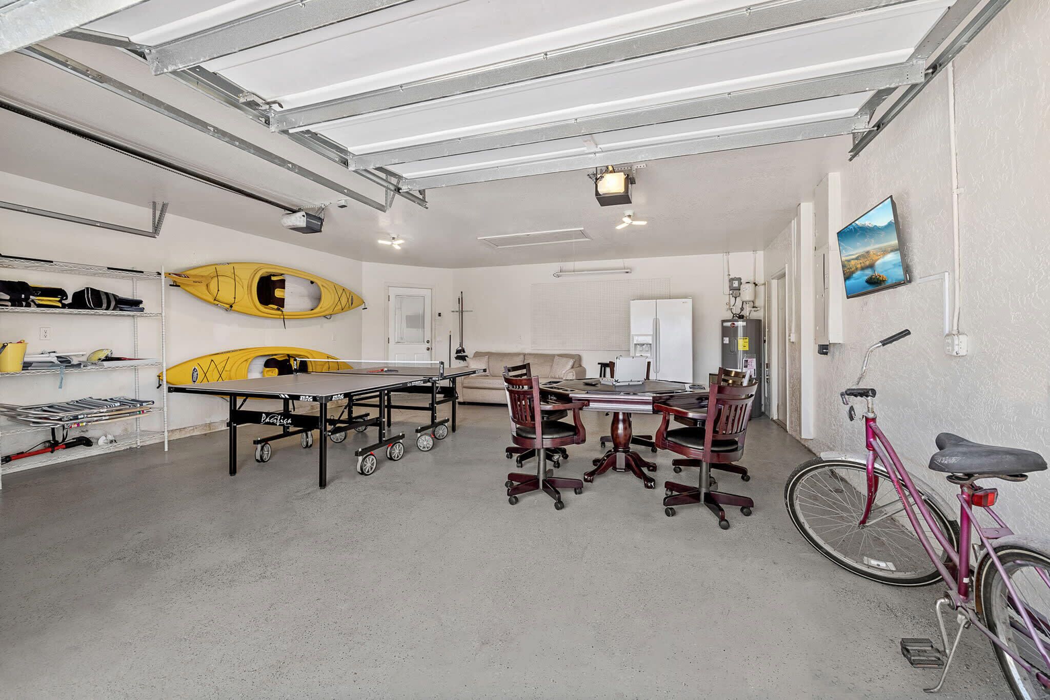 A spacious indoor area with a table and chairs, a bicycle, kayaks, and a refrigerator.