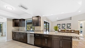 A modern kitchen with dark cabinetry, granite countertops, and a built-in dishwasher. - Waterfront Paradise with HTD Pool, Kayaks & Games (Cape Coral)