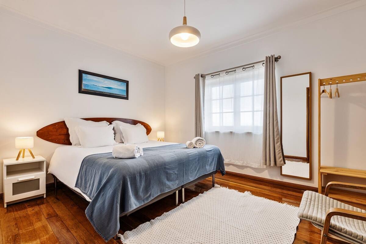 Un dormitorio con cama, mesitas de noche, un espejo y una ventana con cortinas.
