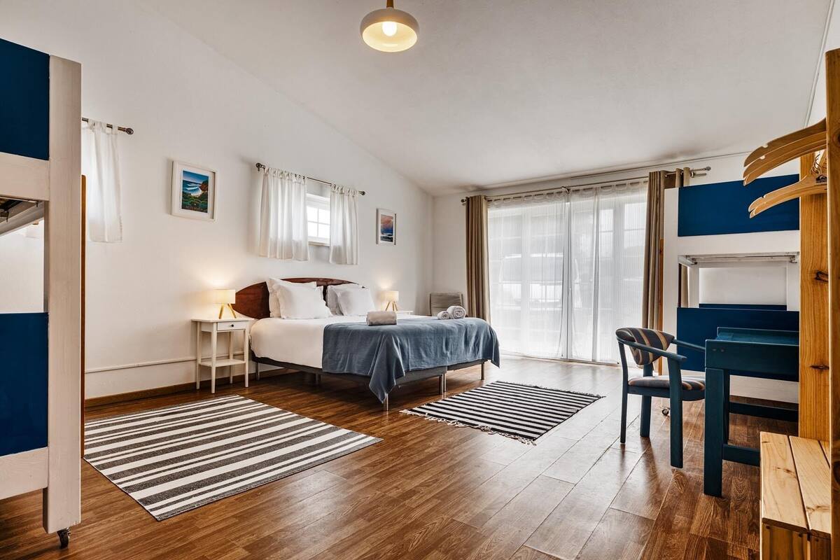 Un dormitorio con cama, mesitas de noche, escritorio, silla y ventana con cortinas.