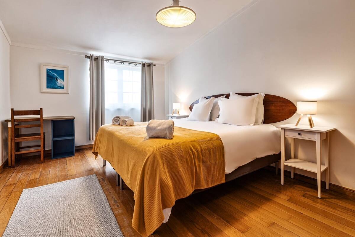 Una habitación de hotel con una cama, un escritorio, una silla, una mesita de noche y una ventana con cortinas.