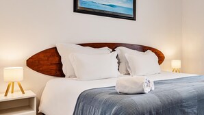 A neatly made bed with a blue and white striped blanket, white pillows, and a framed picture of a beach scene above it. - FreeSurfCamp (Peniche)