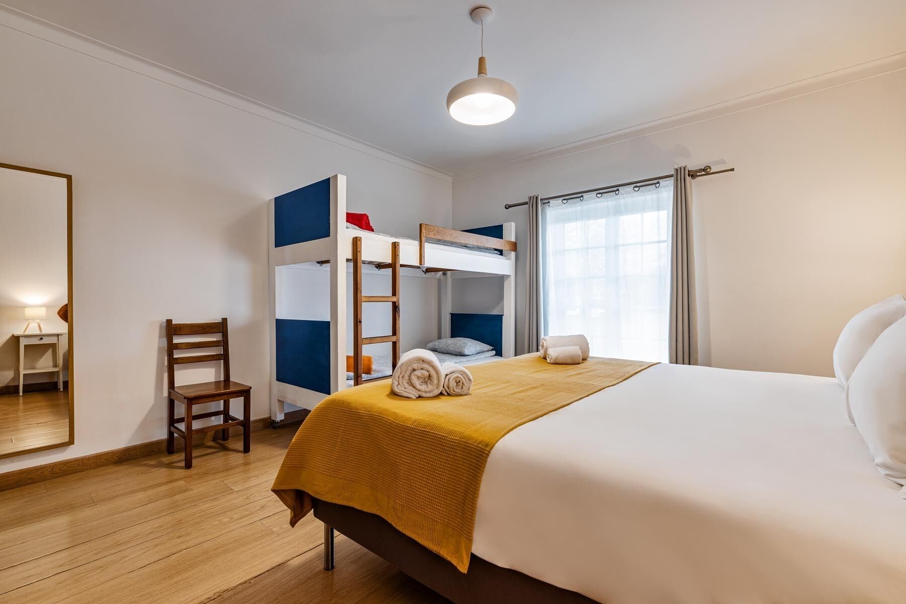 Un dormitorio con una cama individual, una litera, una silla de madera, un escritorio y una lámpara.