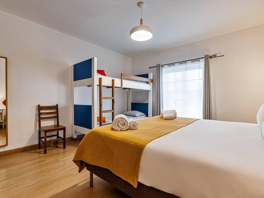 Un dormitorio con una cama individual, una litera, una silla de madera, un escritorio y una lámpara.