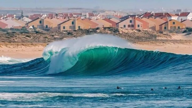 A coastal town with colorful houses and a large wave in the foreground. - FreeSurfCamp (Peniche)