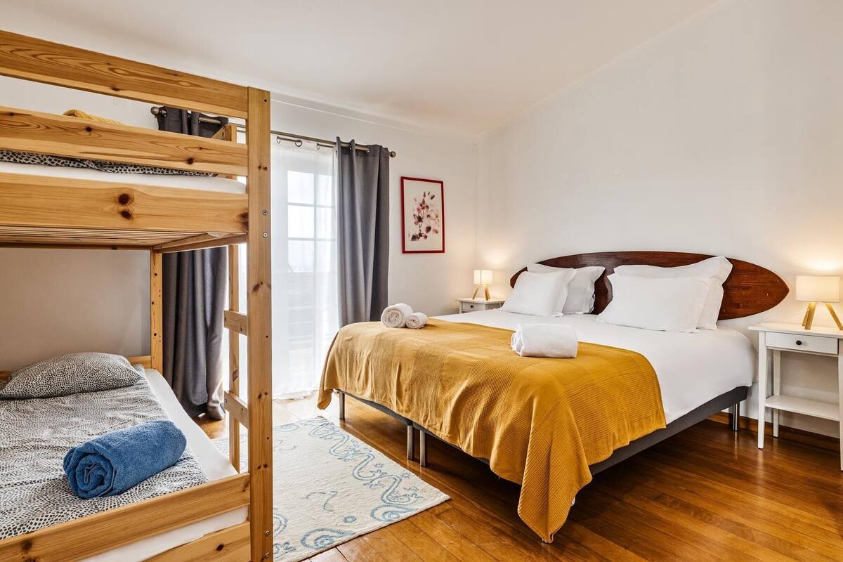 Una habitación con una cama individual, una litera, una mesita de noche, una lámpara y un cuadro en la pared.