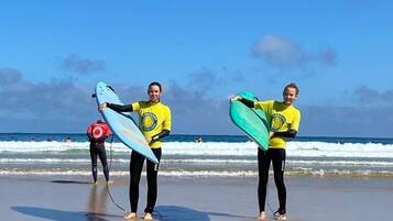 Zwei Personen am Strand mit Surfbrettern, im Hintergrund Wellen.