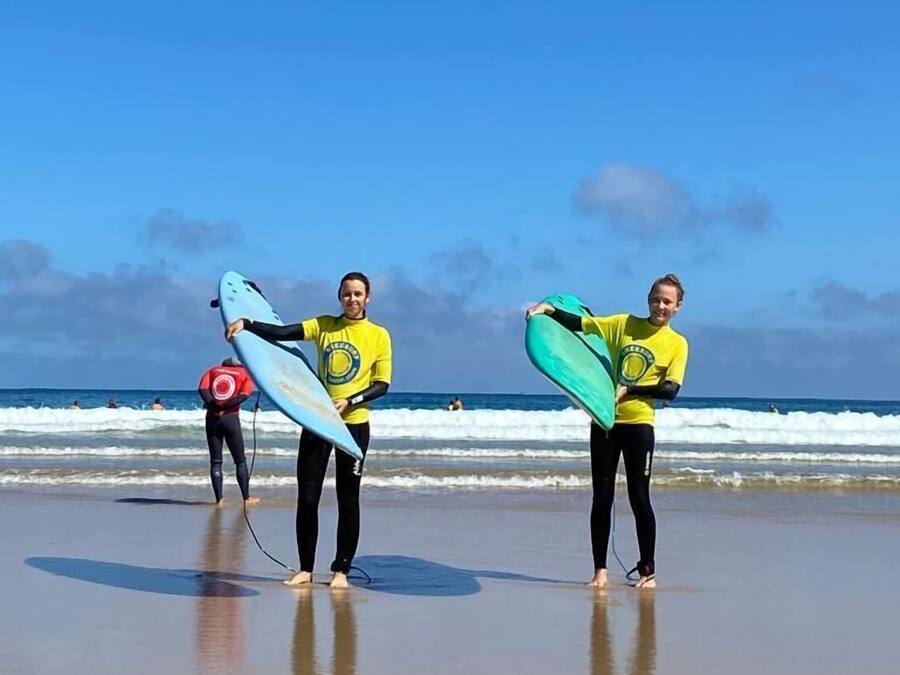 Zwei Personen am Strand mit Surfbrettern, im Hintergrund Wellen.