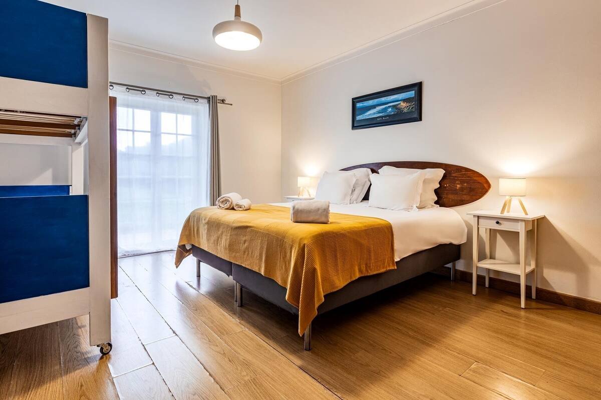 Una habitación de hotel con una cama, una mesita de noche con lámpara, una ventana con cortinas y un cuadro en la pared.