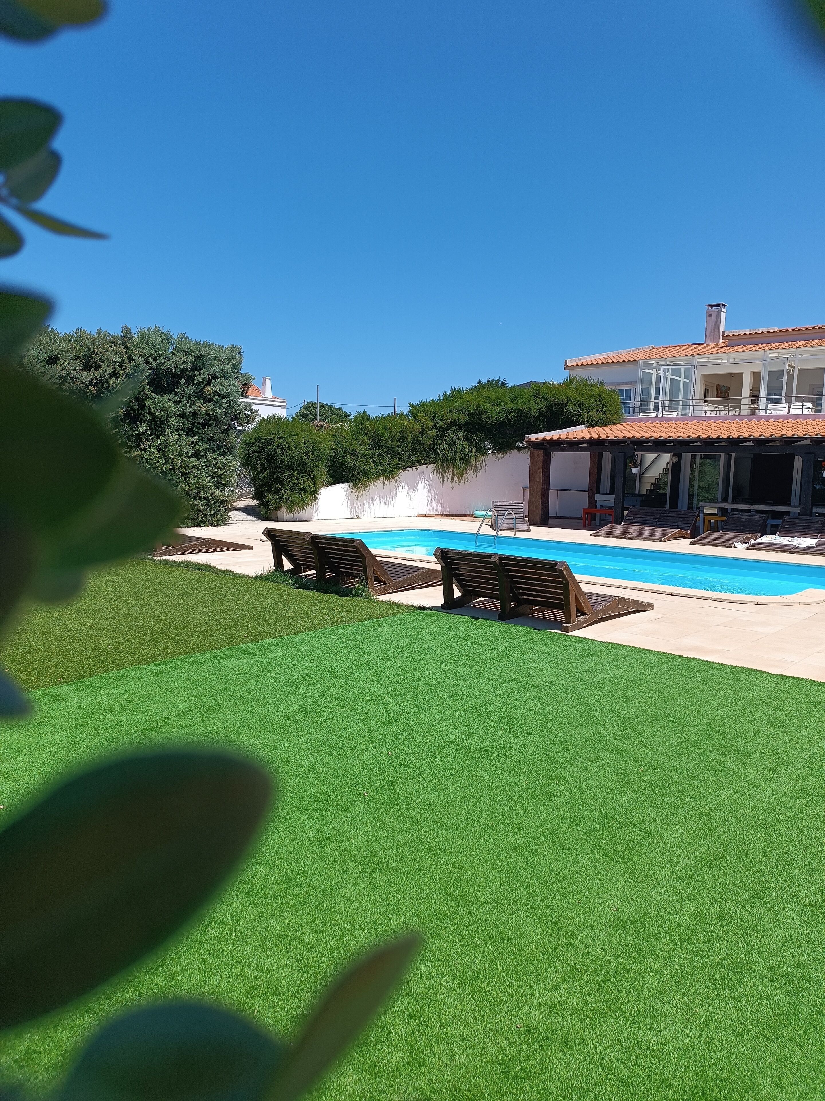 Une piscine à l’eau d’un bleu cristallin, entourée d’une pelouse bien entretenue et de chaises longues en bois.