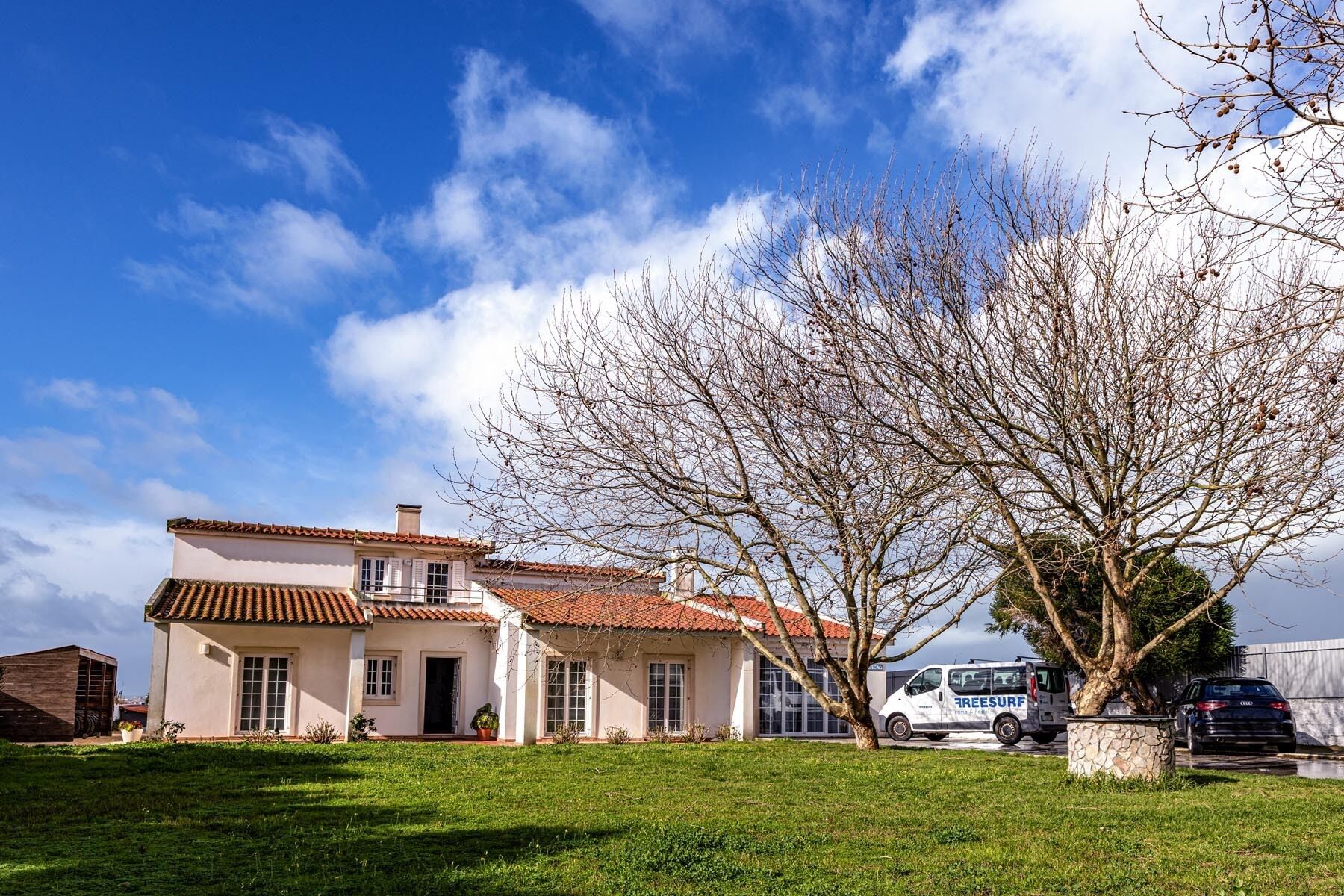 Una casa de dos pisos con techo de tejas, jardín delantero y una furgoneta estacionada.