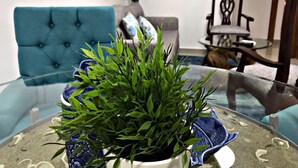 Ein Wohnzimmer mit einem blauen Sofa, einem Glastisch mit Pflanze und einem an der Wand montierten Fernseher.