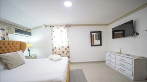 Ein Schlafzimmer mit einem Bett, Nachttisch, Lampe, Vorhängen, einem Schminktisch und einem an der Wand montierten Fernseher.