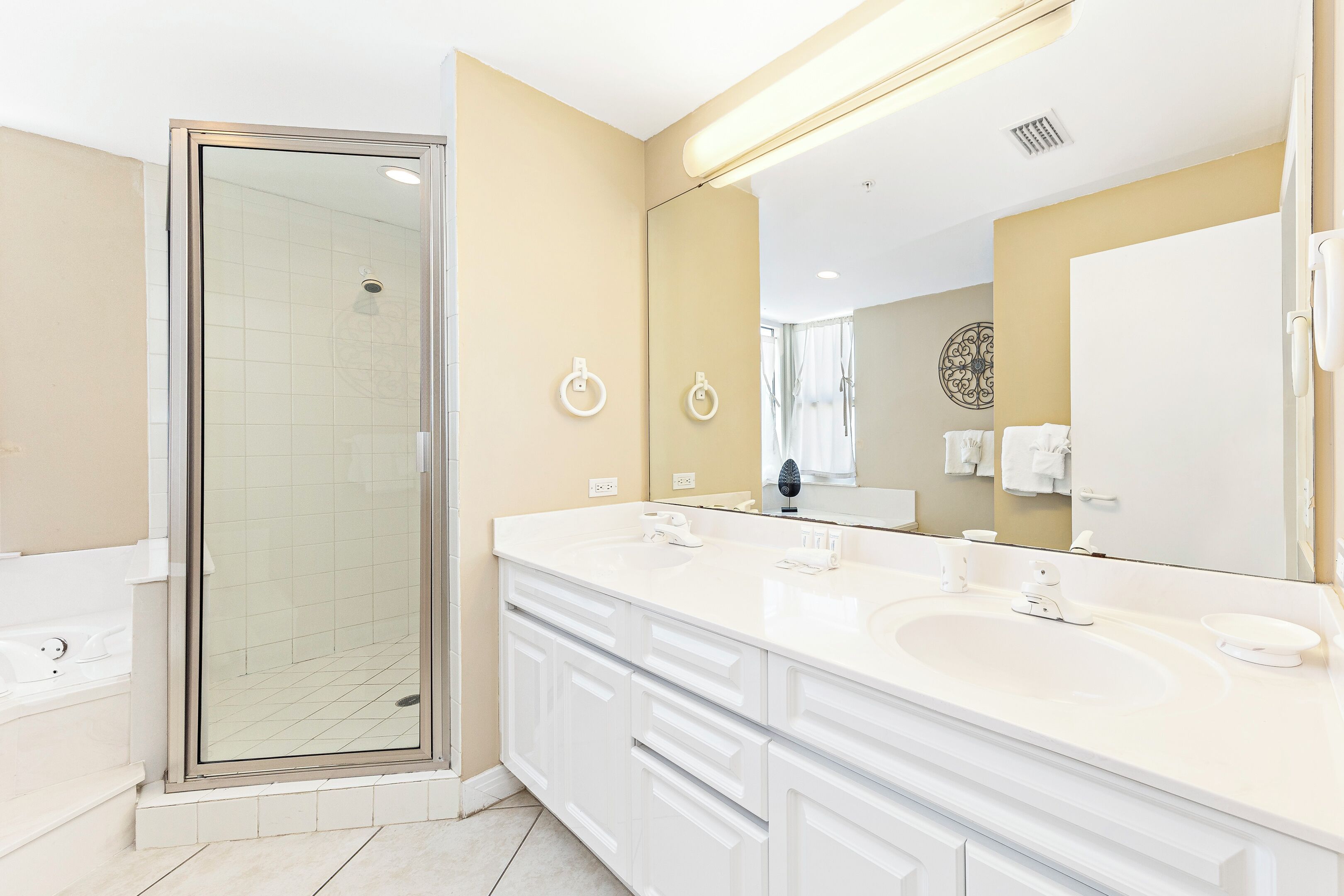 Un baño moderno con ducha envuelta en vidrio, un mueble de tocador grande con dos lavamanos y un espejo amplio.
