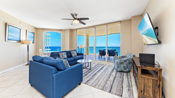 A spacious living room with a blue sofa, a small round table, and a TV on a wooden stand. - Beach Colony E10B (Pensacola)