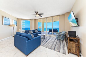 A spacious living room with a blue sofa, a small round table, and a TV on a wooden stand. - Beach Colony E10B (Pensacola)