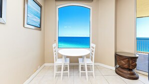 A room with a view of the ocean, a round table with chairs, and a small side table. - Beach Colony E10B (Pensacola)