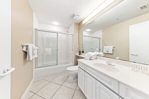 A modern bathroom with a glass-enclosed shower, a white toilet, and a large vanity with a mirror. - Beach Colony E10B (Pensacola)