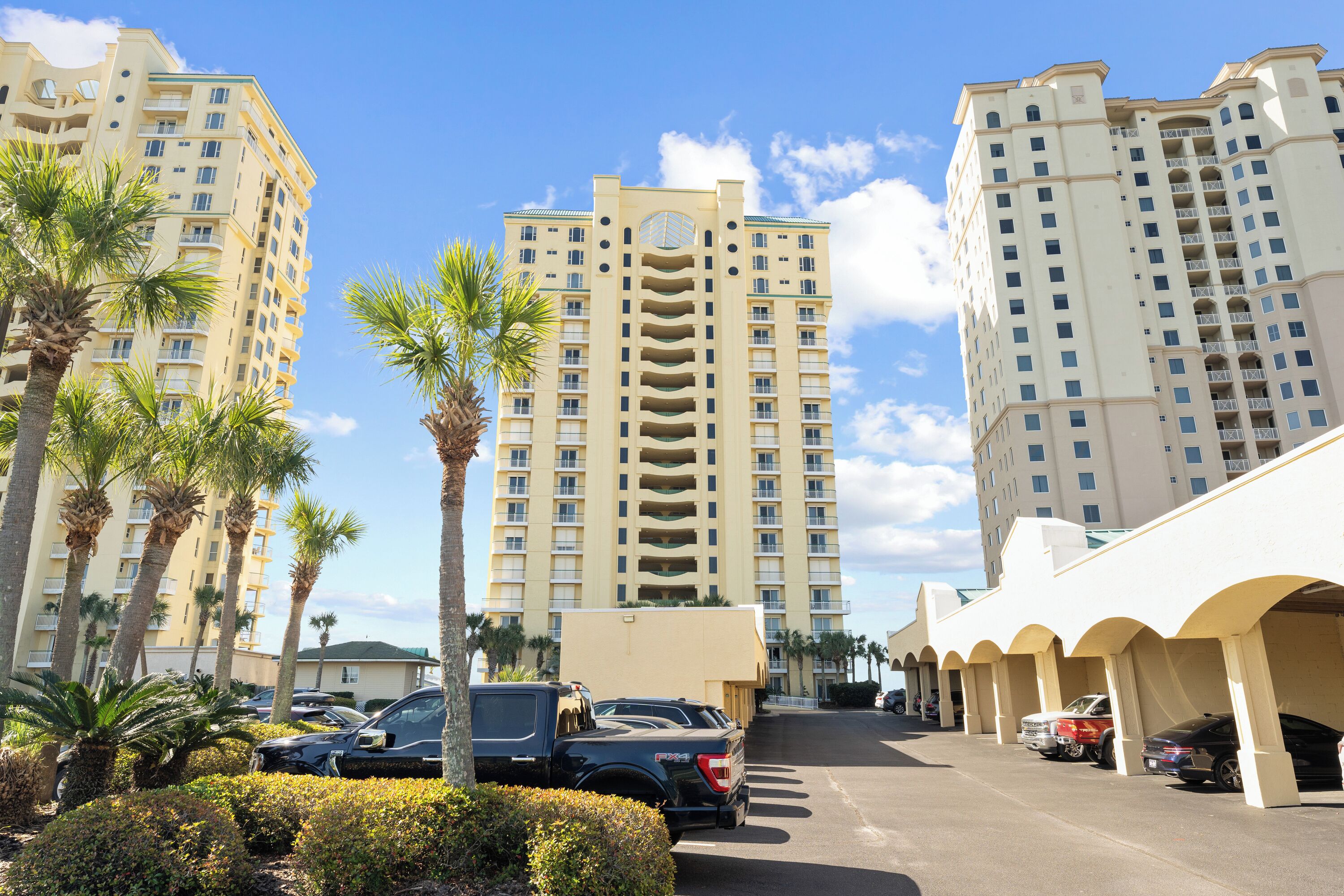 A multi-story hotel with a central atrium, parking area, and palm trees.