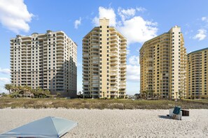 A beachfront hotel with multiple high-rise buildings, a sandy beach, and a clear sky. - Beach Colony E10B (Pensacola)