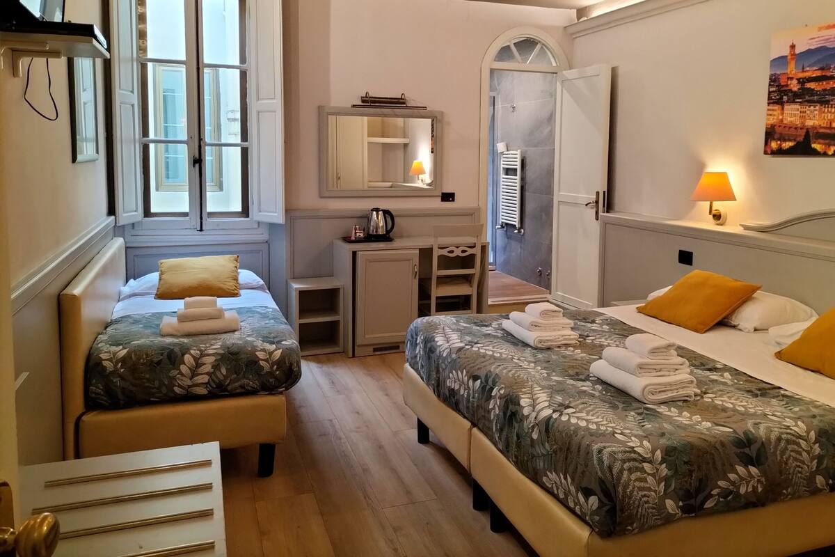 A hotel room with two beds, a desk, a mirror, and a shower.