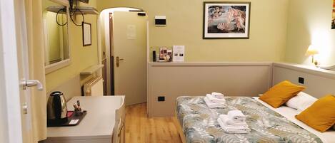 Habitación de hotel con cama, escritorio, silla, radiador, televisor y un cuadro en la pared.