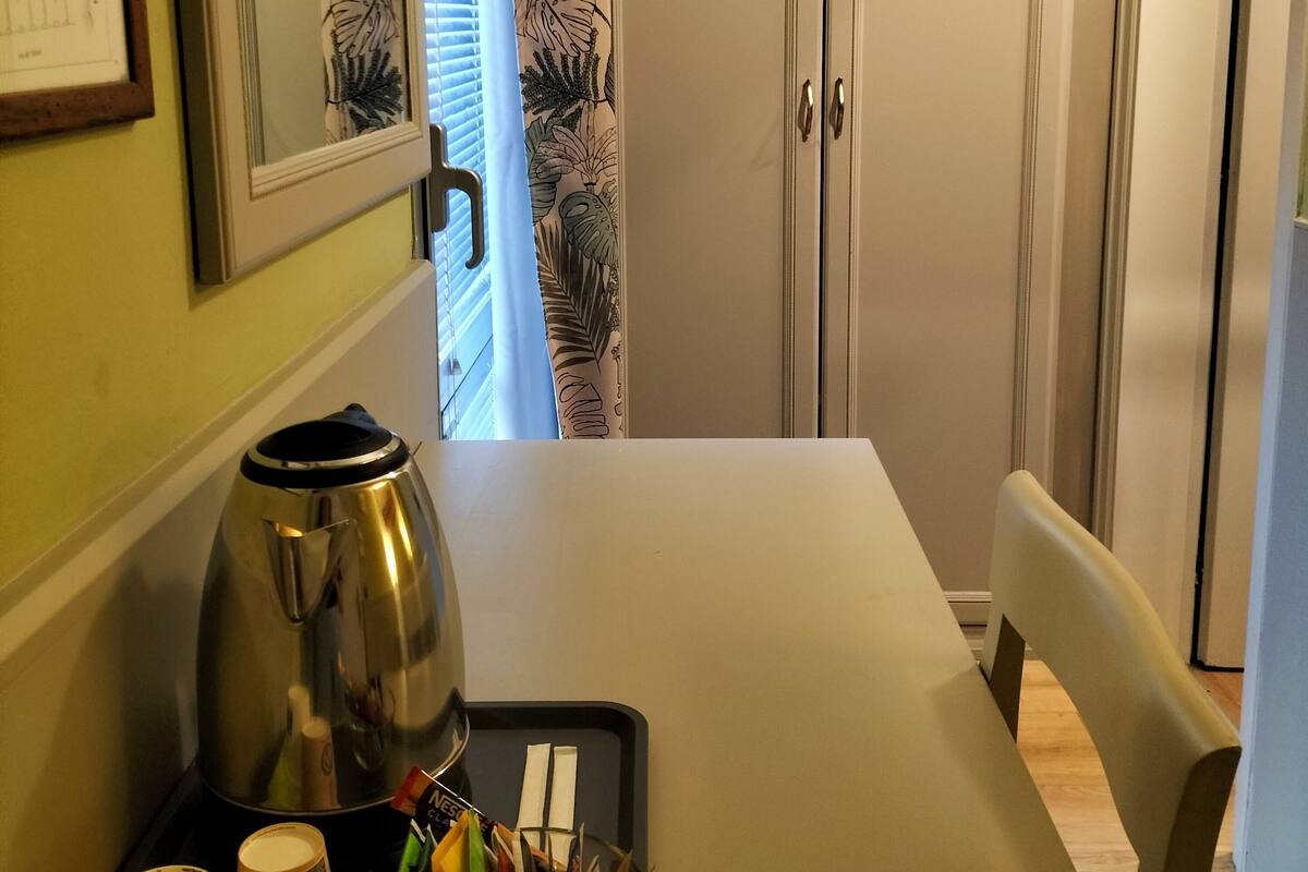 A dining area with a table set for two, a kettle, and a tray with cups and utensils.