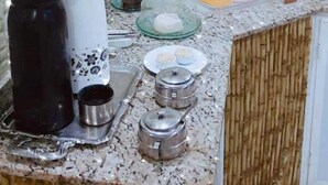 A kitchen with a granite countertop, a coffee maker, a kettle, and a glass shelf with various items. - POUSADA PONTA DO ARPAO (Mangaratiba)