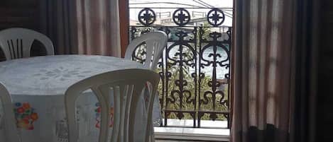 A dining area with a table and chairs, a view of a balcony with a railing, and a tiled floor.
