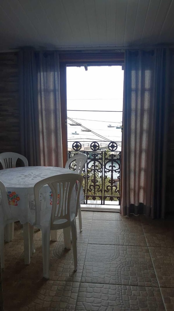 Un comedor con una mesa y sillas, vista a un balcón con barandilla y suelo de baldosas.