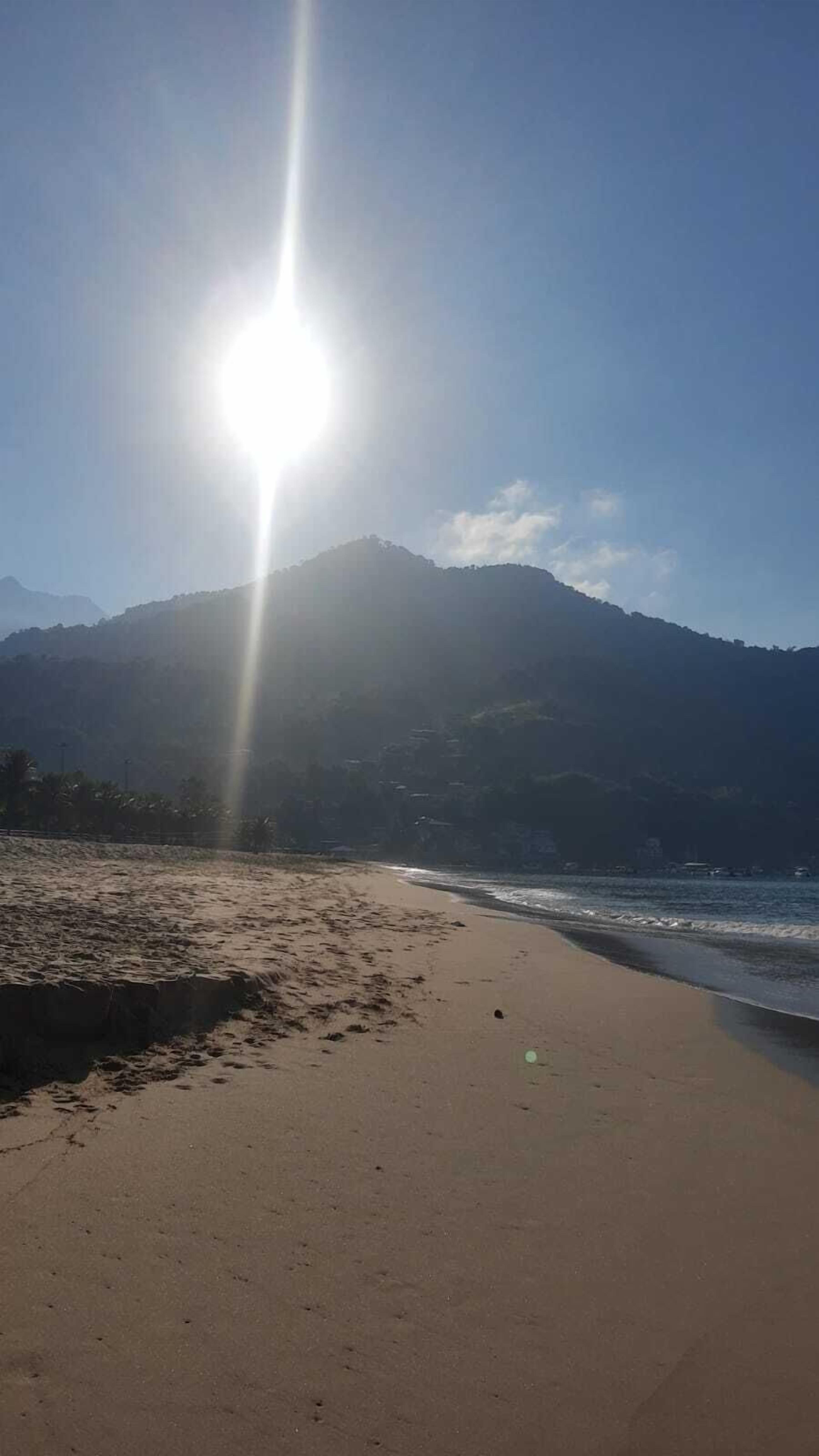 Ein Strand mit einem Berg im Hintergrund und strahlendem Sonnenschein.