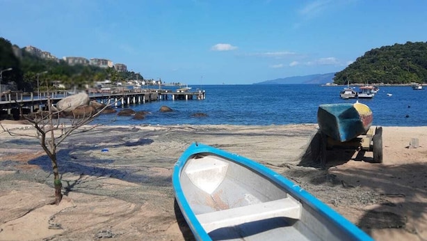 A beach with a small boat, a pier, and a distant hill. - POUSADA PONTA DO ARPAO (Mangaratiba)