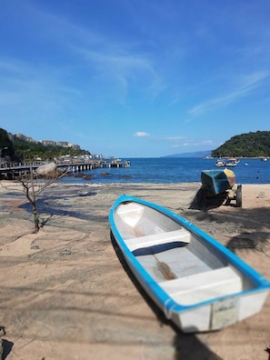 Una playa con un bote pequeño, un muelle y una colina distante.