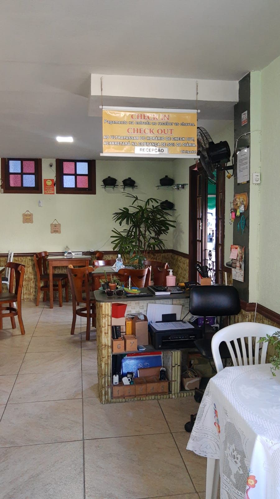 A restaurant with a check-in/check-out counter, tables, chairs, and a small office area with a computer and printer.