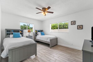 Cozy retreat with two single beds, a ceiling fan, and a view of lush greenery.