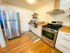 Eine kleine Küche mit Edelstahl-Kühlschrank, Gasherd und weißen Schränken.