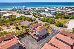 A coastal residential area with multiple two-story houses, a central road, and a beach in the background.