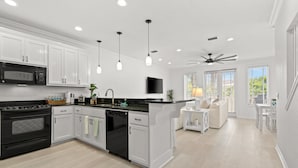 A modern kitchen with white cabinetry, a black stove, and a dishwasher. There is a dining area with a white table and chairs, and a ceiling fan. - Spacious 4BR • Pool • Arcade • Walk to Beach • BBQ (Panama City Beach)