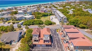 An aerial view of a coastal residential area with multiple two-story houses, a parking lot, and a beach in the background. - Spacious 4BR • Pool • Arcade • Walk to Beach • BBQ (Panama City Beach)