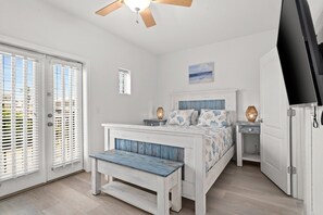 A bedroom with a bed, a bench, a nightstand, a TV, and a door.